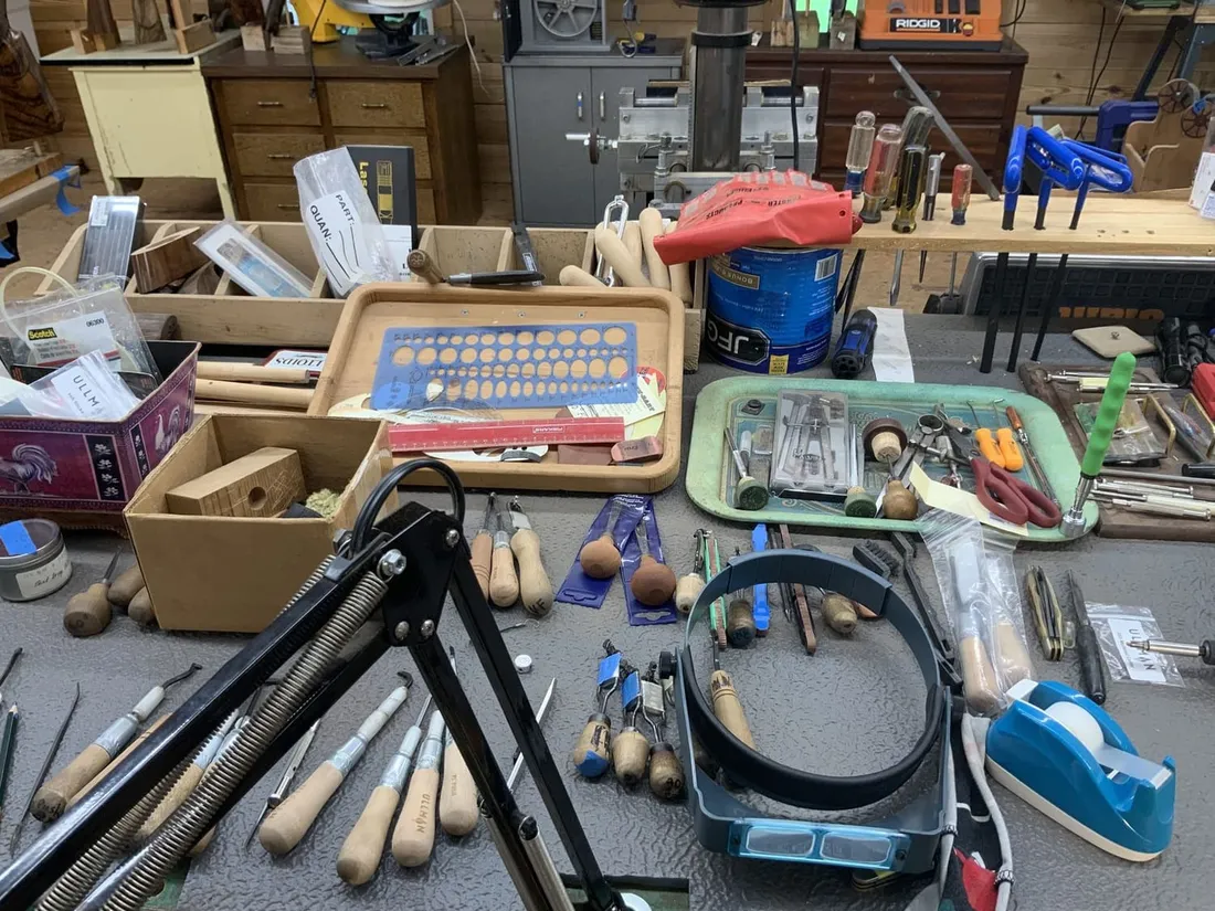 Checkering cradles, files and wooden-handled cutters laid out on the bench beside a magnifier visor